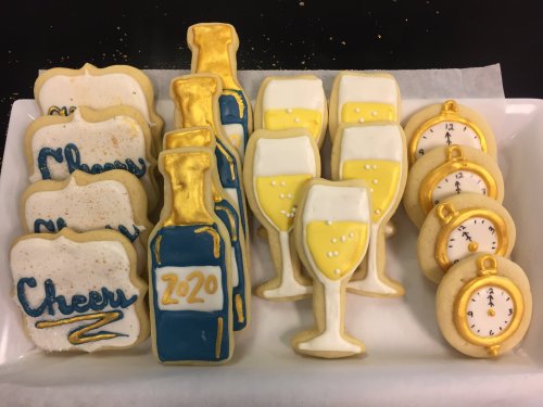 A platter of decorated cookies featuring champagne bottles, glasses, and clock cookies, celebrating New Year's 2020.