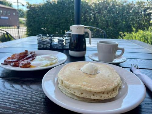 A plate of pancakes with a dollop of cream, a side of bacon and eggs, and a cup of coffee on a wooden table.