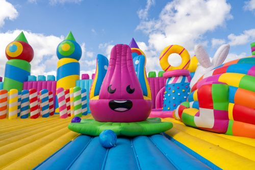 A colorful inflatable bounce house with a smiling purple character, surrounded by vibrant patterns and shapes.