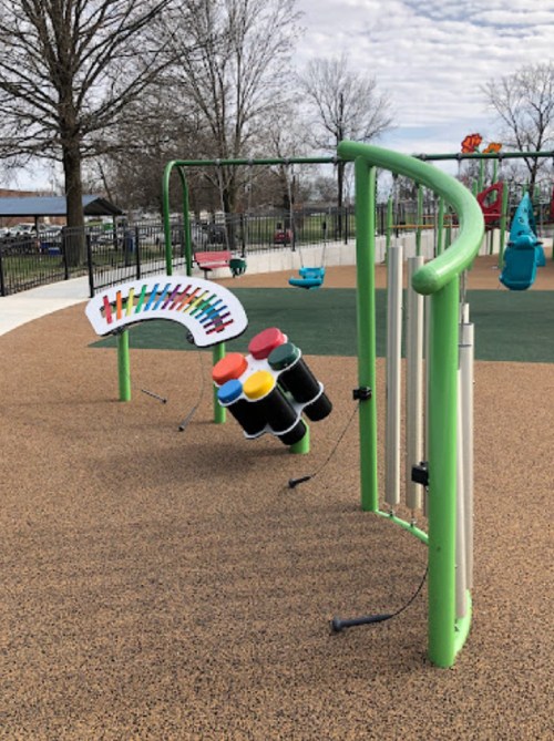 Colorful outdoor musical playground equipment with xylophone and large tubes on a rubber surface. Trees in the background.