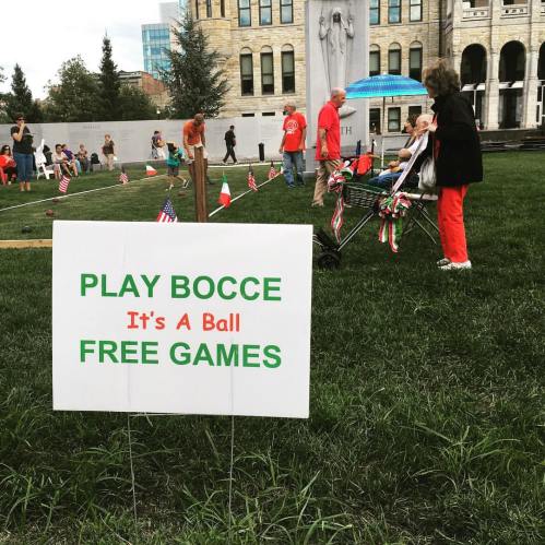 A sign reads "Play Bocce It's A Ball Free Games" with people playing bocce and enjoying a festive atmosphere.