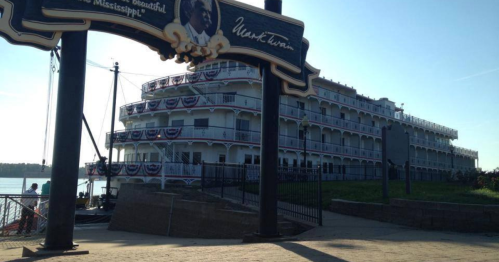 A large riverboat docked by the shore, adorned with patriotic bunting and a sign featuring Mark Twain's name.