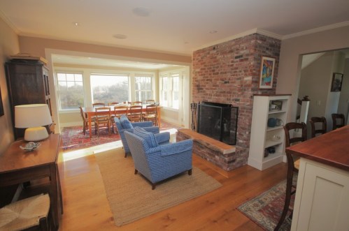 Cozy living space with blue chairs, a brick fireplace, and a dining area with large windows overlooking nature.