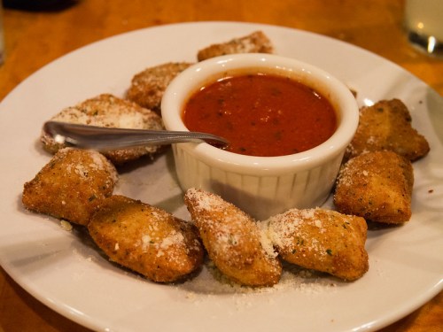 A plate of golden-brown fried snacks arranged around a small bowl of marinara sauce, sprinkled with cheese.
