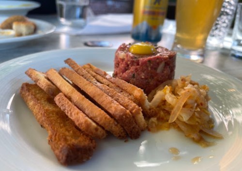 A plate with toasted bread strips, a meat tartare topped with an egg yolk, and a side of coleslaw.