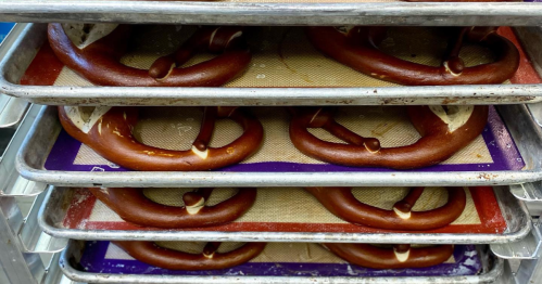 Freshly baked pretzels cooling on trays lined with silicone mats.