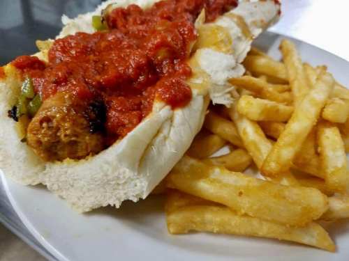 A hot dog topped with marinara sauce and peppers, served with a side of golden French fries on a white plate.