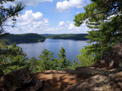 A serene lake surrounded by lush greenery and trees, under a partly cloudy sky.