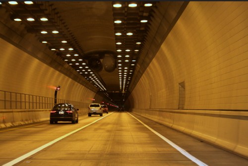 Two cars driving through a well-lit tunnel with a smooth, concrete surface and illuminated ceiling.