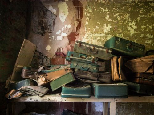 A pile of old, worn suitcases stacked on a shelf in a dilapidated room with peeling walls.