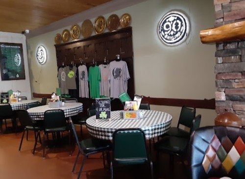 Interior of a restaurant featuring checkered tables, green chairs, and wall decor with t-shirts and circular signs.