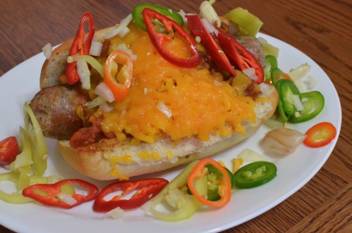 A loaded hot dog topped with melted cheese, sliced peppers, and onions on a white plate.