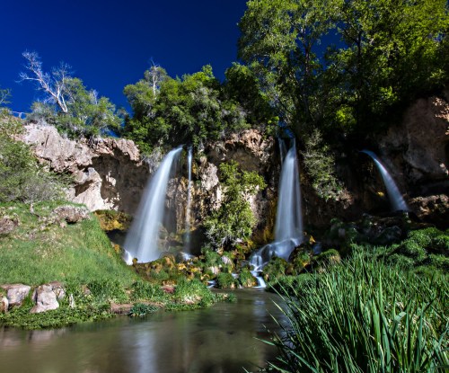 A serene landscape featuring cascading waterfalls surrounded by lush greenery and a clear blue sky.