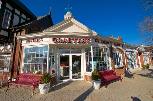 A charming storefront of Graeter's featuring ice cream and pastries, with red benches outside and a clear blue sky.