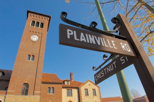 Signpost for Plainville Rd and Chestnut St with a clock tower in the background against a clear blue sky.