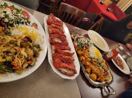 A table spread with colorful dishes: lobster, rice, salad, grilled vegetables, and sauces in a restaurant setting.