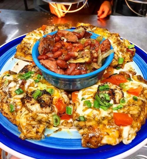 A colorful plate of cheesy nachos topped with shrimp, tomatoes, and green onions, served with a side of beans and sausage.