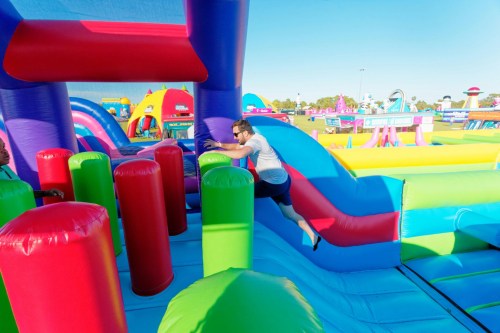 A person jumps over colorful inflatable obstacles at a vibrant outdoor bounce park.