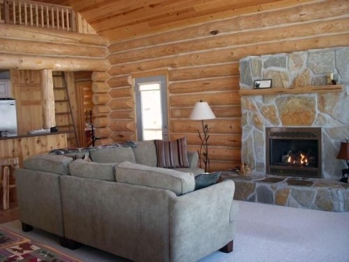 Cozy log cabin interior featuring a stone fireplace, plush sofa, and wooden accents. Warm and inviting atmosphere.