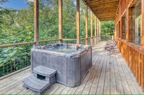 A wooden deck with a hot tub and two lounge chairs, surrounded by lush greenery.