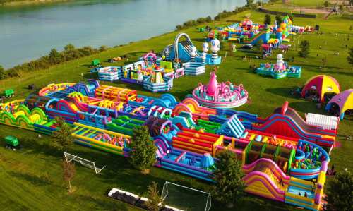 Aerial view of a colorful inflatable amusement park with various slides and obstacle courses by a river.