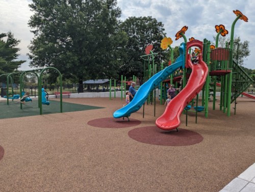 Colorful playground with two slides, climbing structures, and children playing on a sunny day.