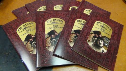 A stack of "Big River Steampunk Festival 2015 Compendium" booklets with ornate covers featuring vintage-style illustrations.