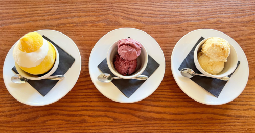 Three dessert bowls on white plates: lemon sorbet, berry sorbet, and vanilla ice cream, each on a black napkin.