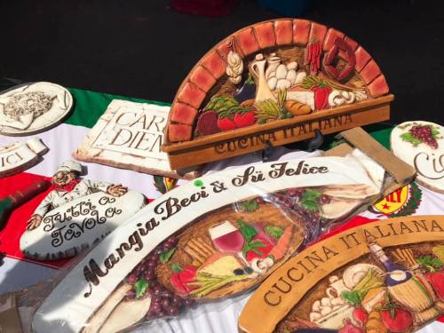 A display of decorative wooden signs featuring Italian food themes and phrases, set on a colorful tablecloth.