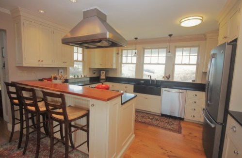 Bright kitchen with white cabinets, a central island with bar stools, and stainless steel appliances.