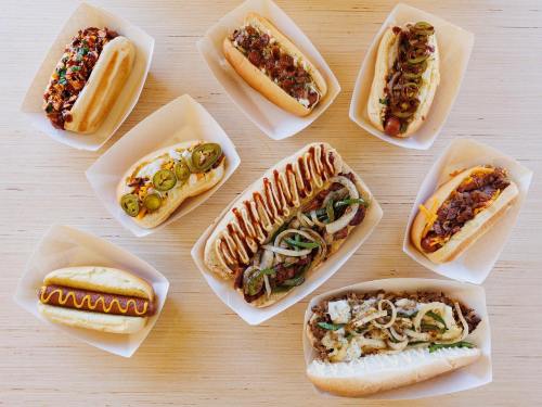 A variety of hot dogs with different toppings arranged in paper trays on a wooden surface.