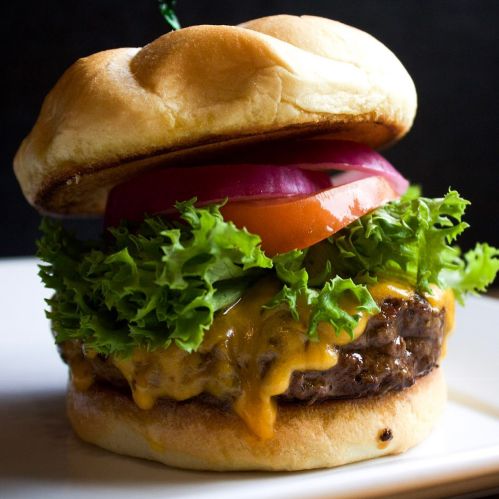 A juicy cheeseburger with melted cheese, lettuce, tomato, and red onion on a toasted bun, served on a plate.