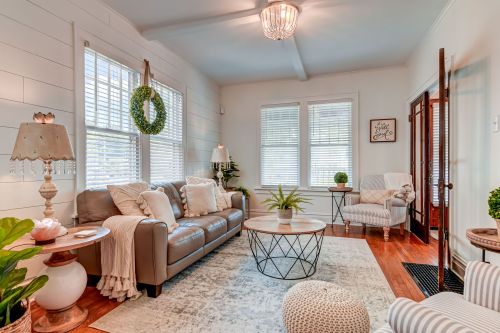 Cozy living room with a leather sofa, round coffee table, plants, and bright windows, featuring a warm, inviting decor.