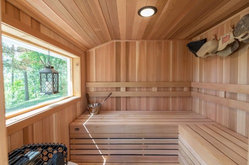 A wooden sauna interior with benches, a lantern, and a window overlooking greenery.