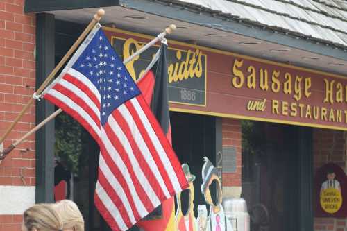 A U.S. flag and a German flag outside a restaurant with a sign reading "Schmidt's Sausage Haus und Restaurant."