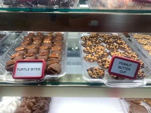 A display case with two types of chocolates: Turtle Bites with pecans and Peanut Butter Cups with chocolate and peanut toppings.