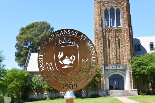 A bronze seal of the University of Arkansas at Monticello in front of a historic building with a clock tower.