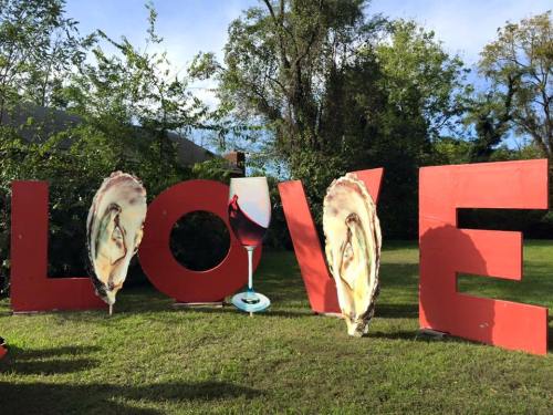Large red letters spelling "LOVE," featuring oyster images and a wine glass, set in a green outdoor space.