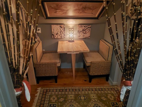 Cozy nook with a wooden table, two chairs, and decorative curtains, illuminated by a soft lamp.