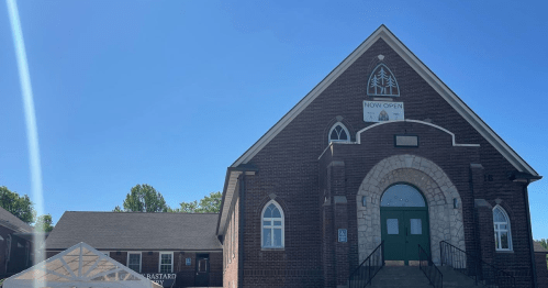 A brick church building with a large entrance, clear blue sky, and a sign that says "Now Open."