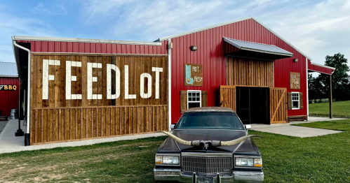 A red barn-style building with "FEEDLOT" on the side and a vintage car with horns parked in front.