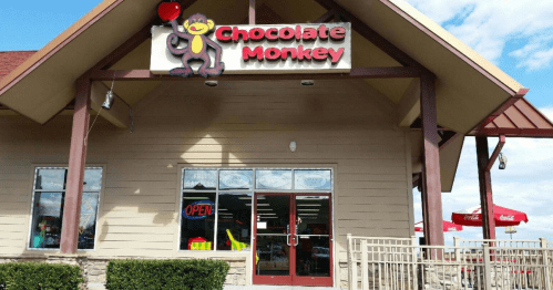 Exterior of a building with a sign reading "Chocolate Monkey," featuring a cartoon monkey and an open sign.
