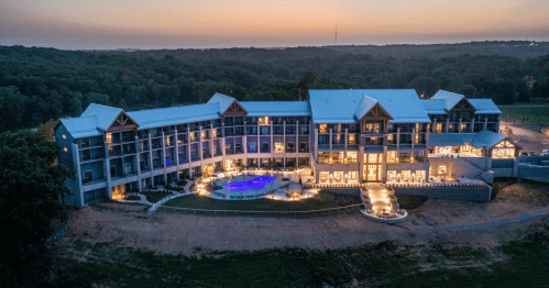 Aerial view of a modern hotel with a pool, surrounded by trees at sunset.