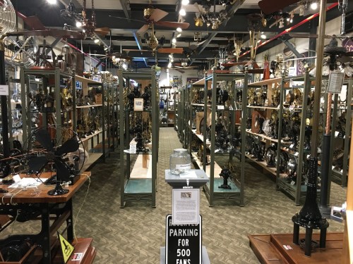 A museum display featuring numerous vintage fans arranged on shelves, with a sign indicating parking for 500 fans.