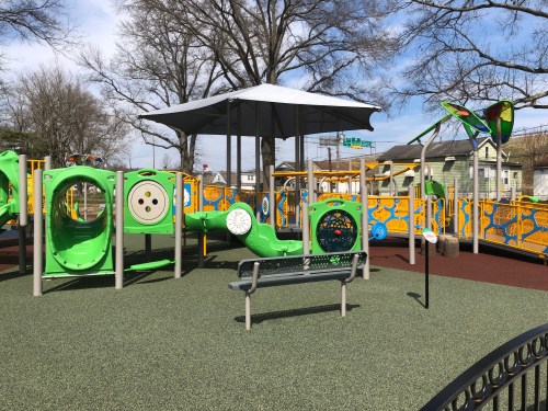 Colorful playground with green equipment, a shaded area, and a bench, set against a clear blue sky.