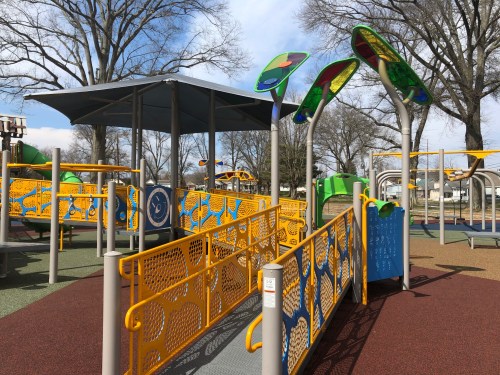 Colorful playground equipment with unique designs, surrounded by trees and a clear blue sky.