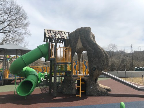Playground structure resembling a tree with slides and climbing features, set in a sunny outdoor area.