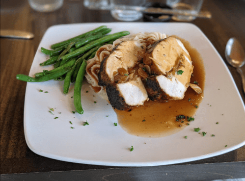 A plate of sliced chicken breast with gravy, served with green beans and mashed potatoes, garnished with herbs.