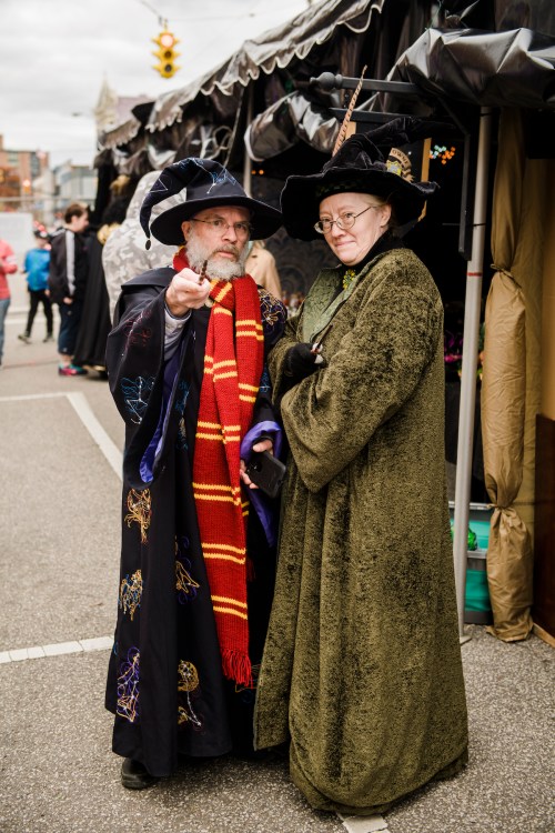 Two people in elaborate wizard costumes stand together, one wearing a colorful scarf and the other in a green cloak.