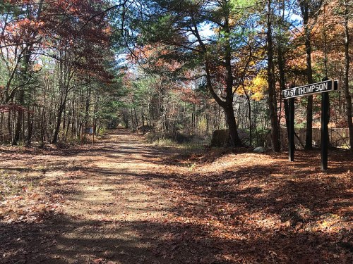 A dirt path lined with trees in autumn, featuring a sign that reads "East Thompson."
